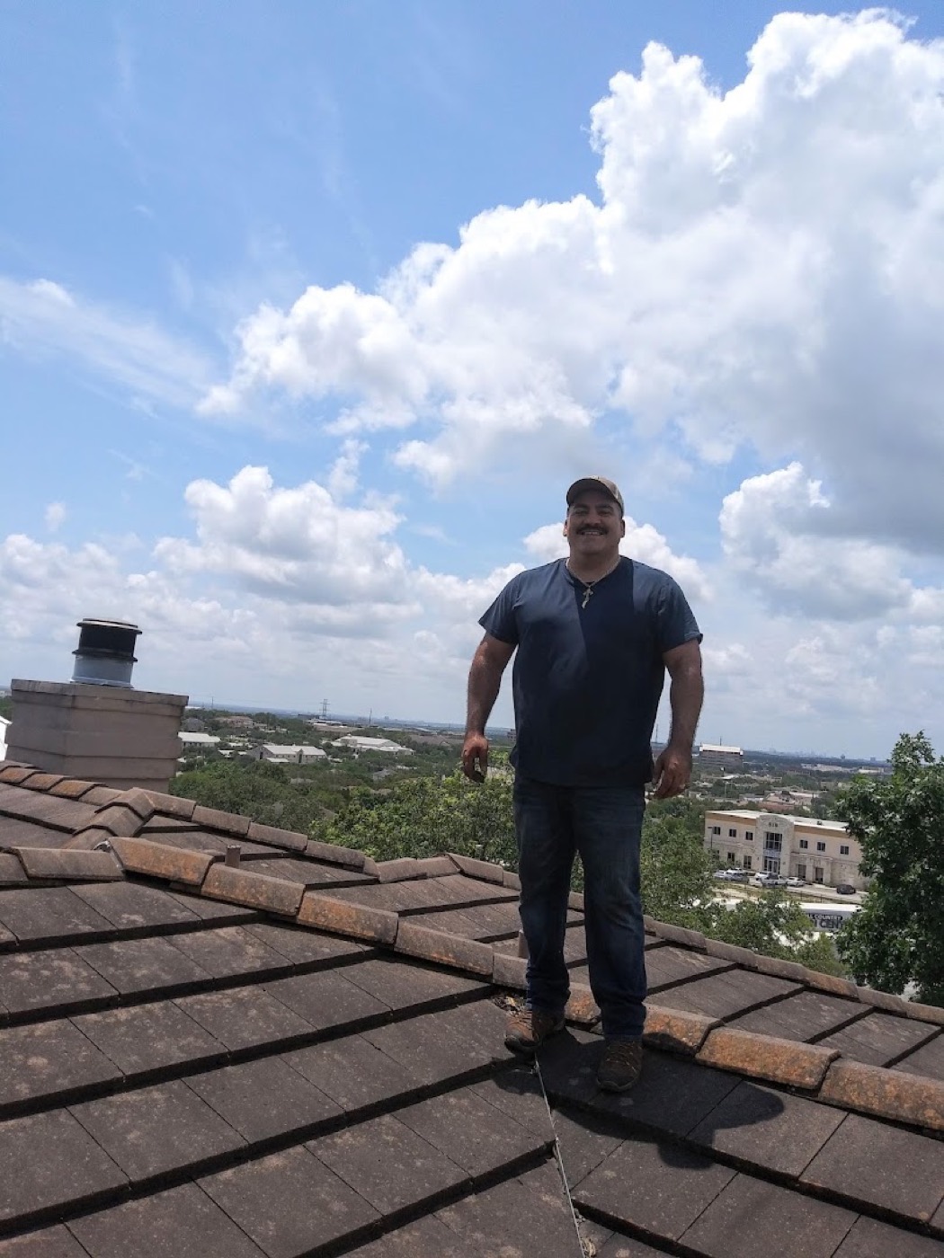 Hugo Guerra standing on a tile roof with the San Antonio skyline behind him